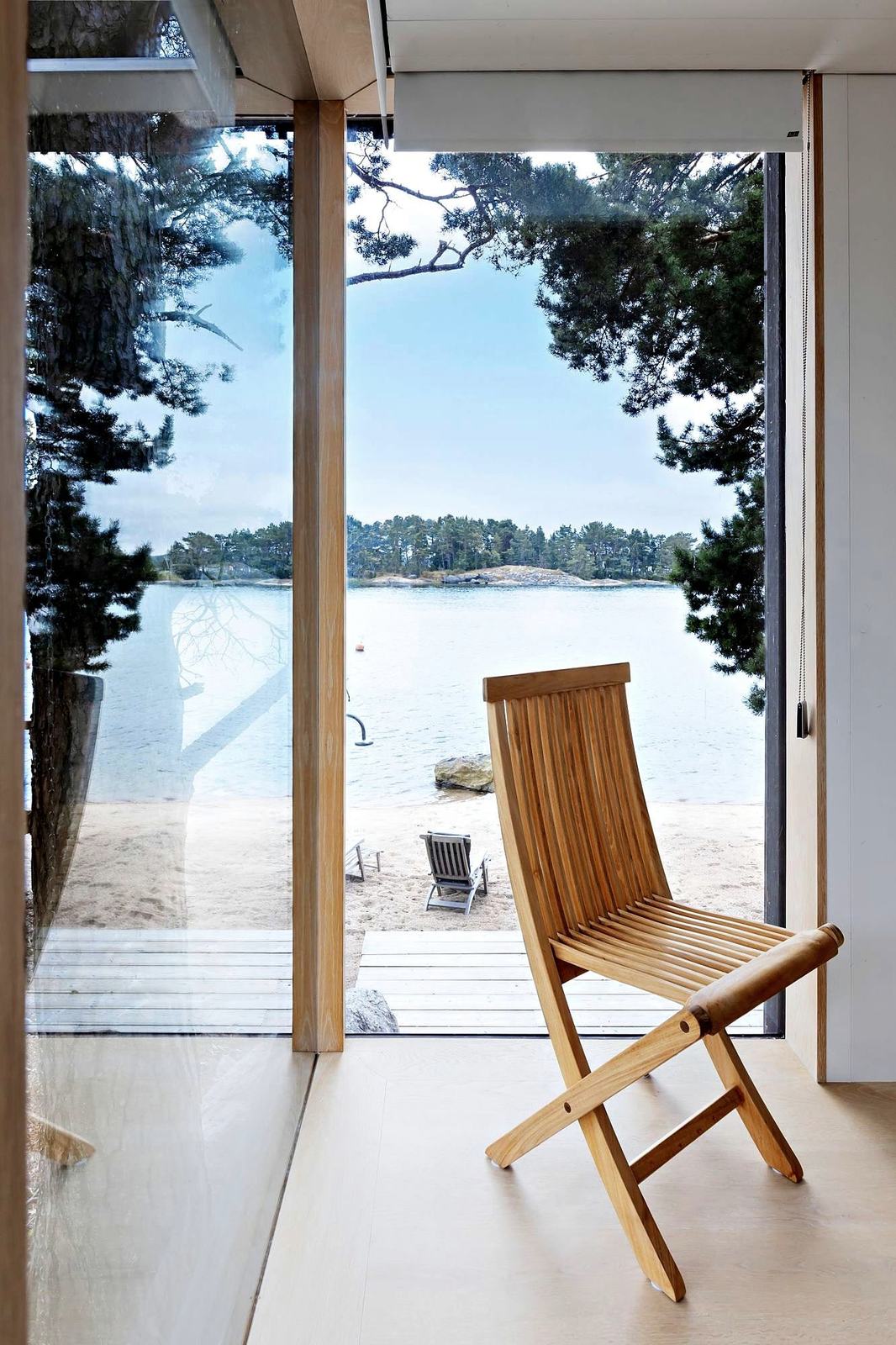 A wooden chair at a glass wall, the sandy beach and the sea beyond