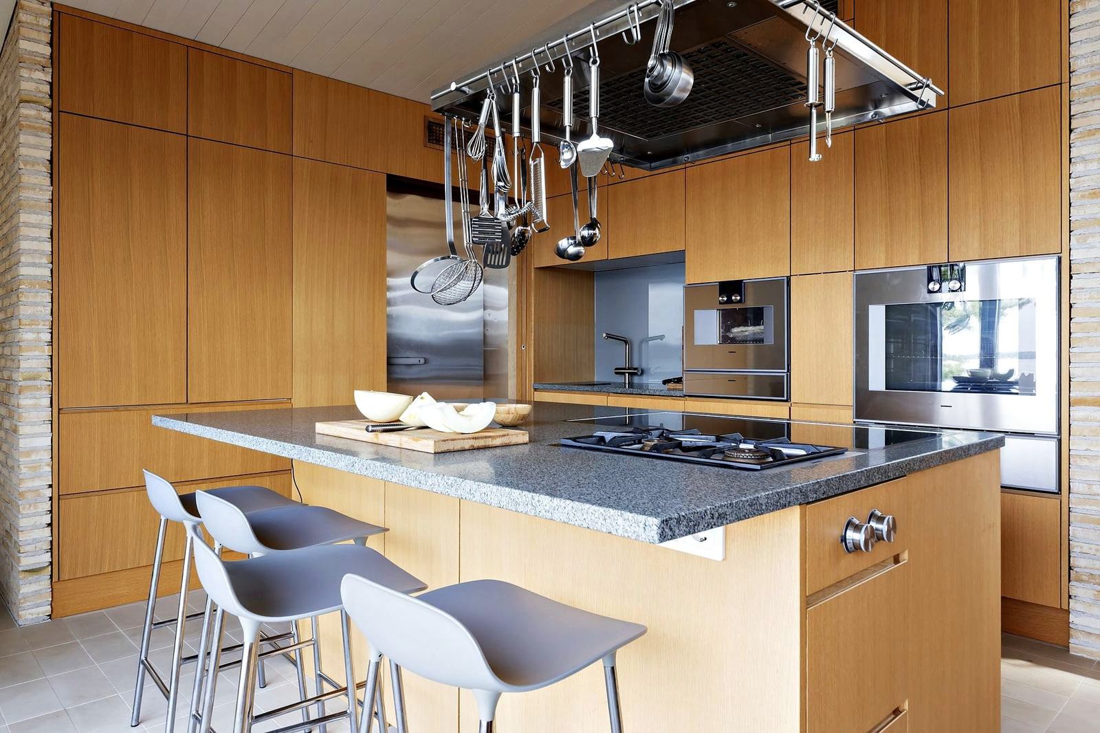An oak kitchen with a granite island, gas hob and hanging copper and steel pans