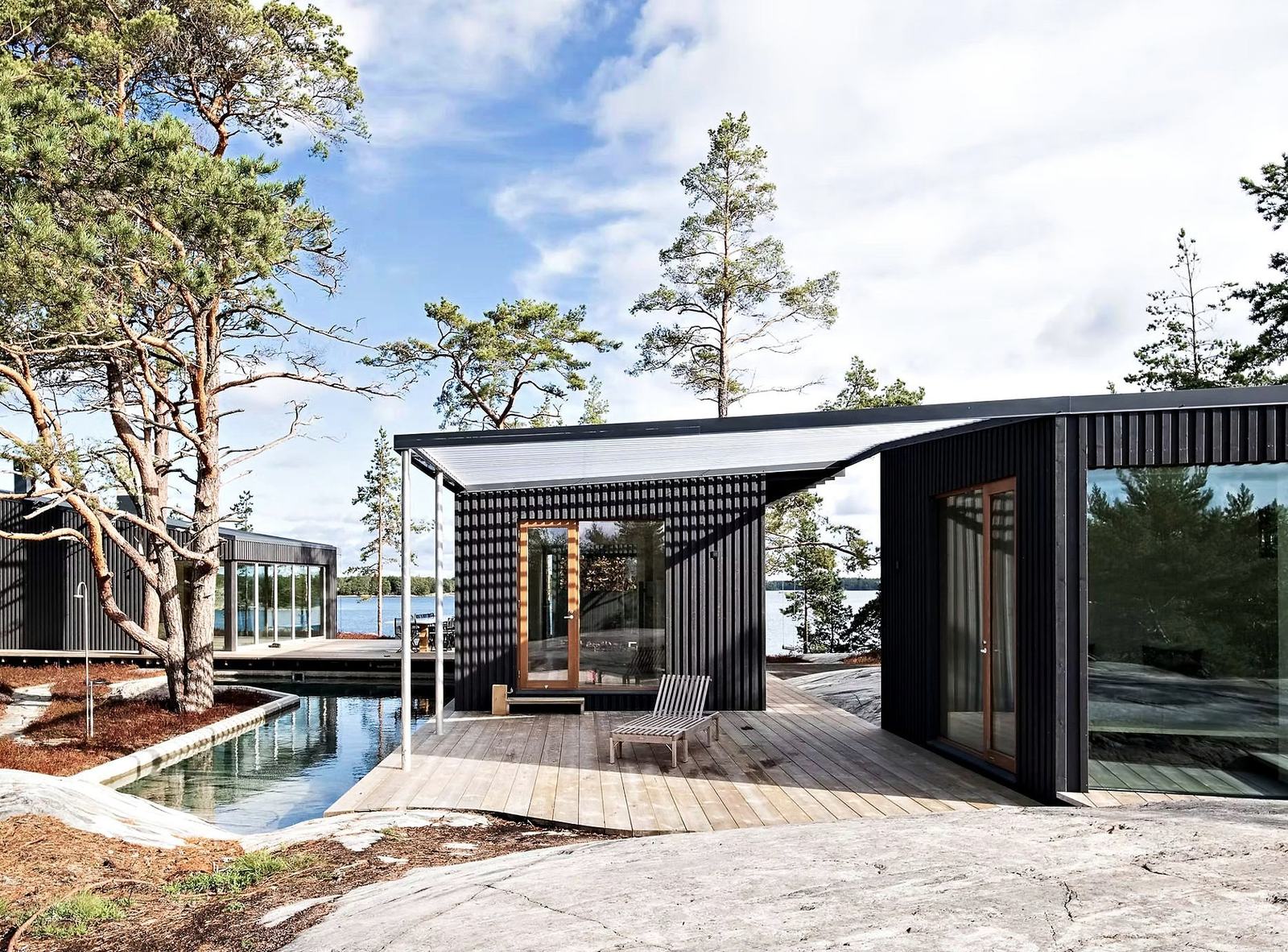 Black timber pavilions and a stone pool on smooth granite, old pines and the sea beyond